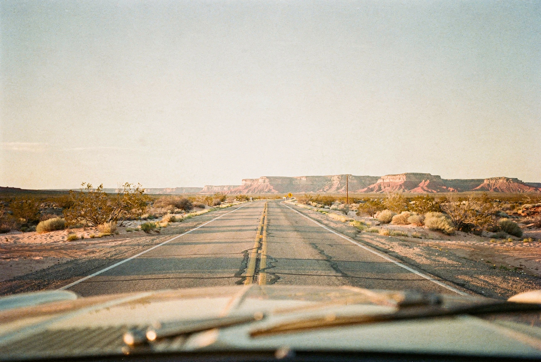 Road trip aux États-Unis : comment rester connecté sans se ruiner ? Route déserte du sud-ouest américain filant vers des mesas rouges au coucher du soleil