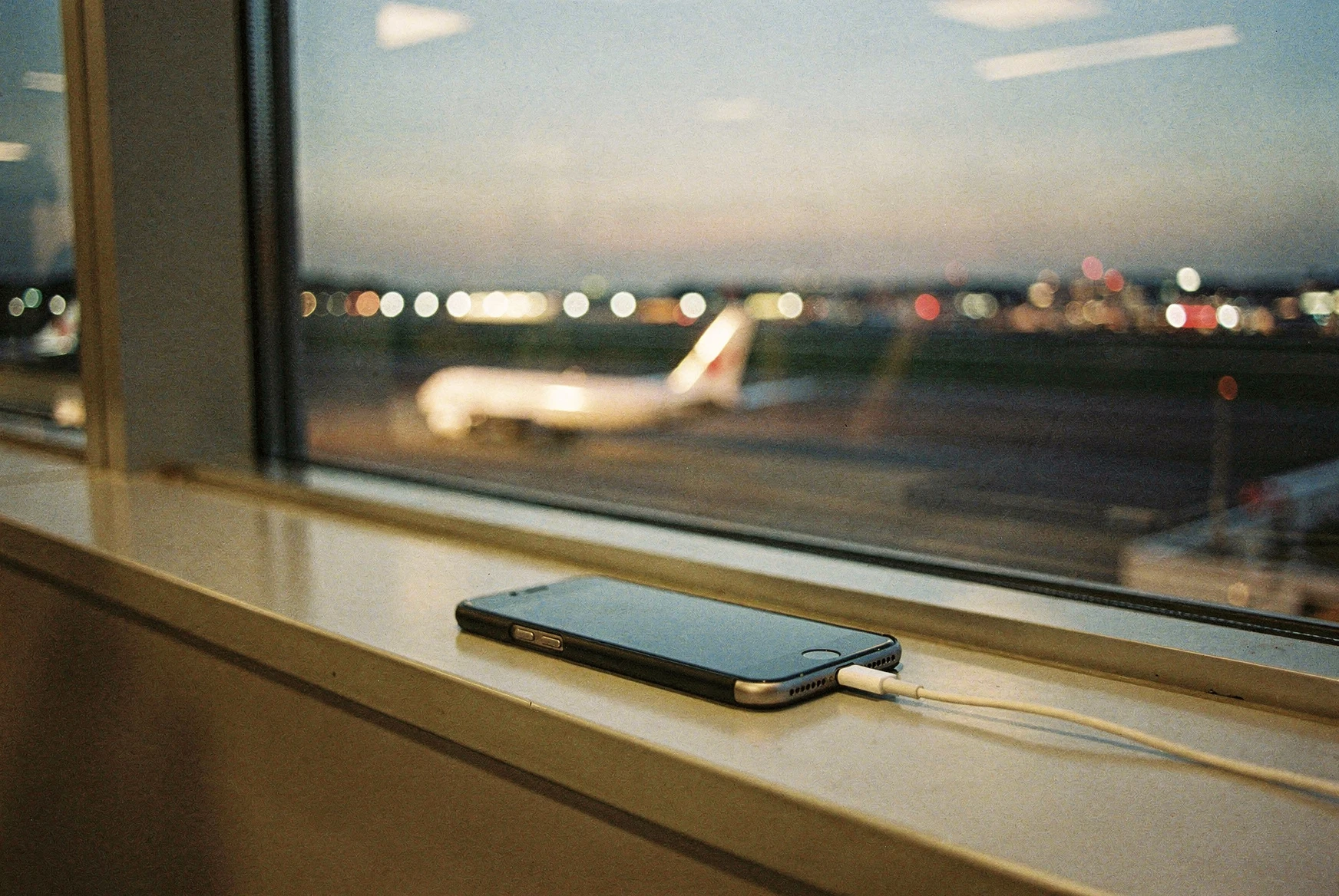 Baie vitrée d'un salon d'aéroport au crépuscule, téléphone en charge sur le rebord